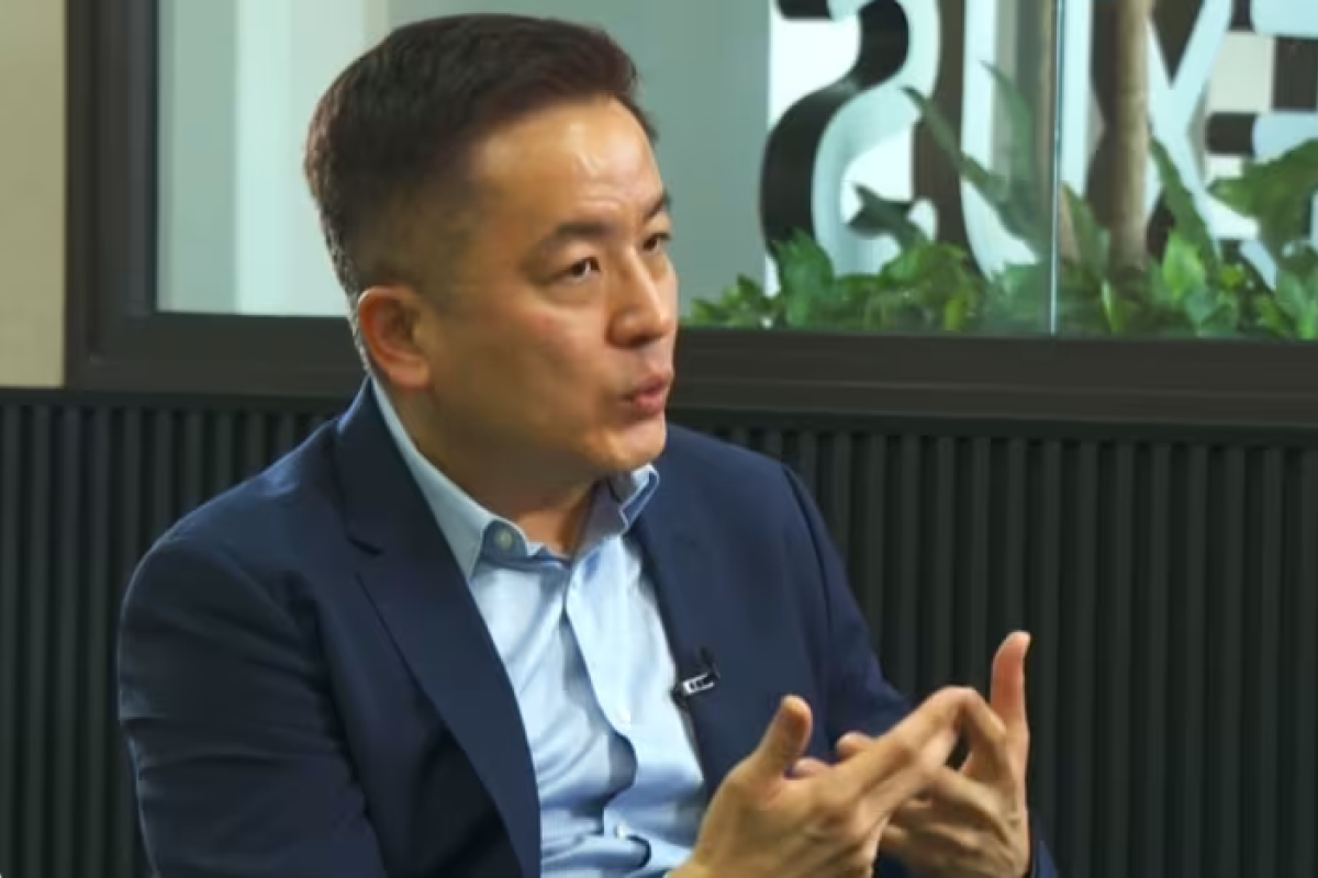 Man speaking during an indoor interview, gesturing in a modern office setting.